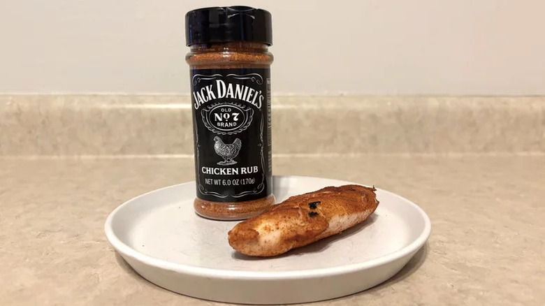 Ένα μπουκάλι από κοτόπουλο Jack Daniel στεγνό τρίψιμο δίπλα σε μια λευκή πλάκα με ένα μαριναριστικό κομμάτι κοτόπουλου
