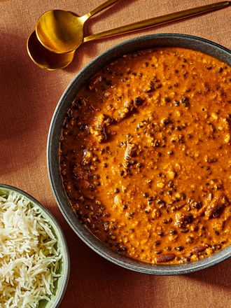 Dal Makhani σε ένα μπολ με 2 χρυσά κουτάλια και 2 κύπελλα ρυζιού. Καίγεται πορτοκαλί έγχρωμη επιφάνεια και μπλε ποτήρι νερό. 