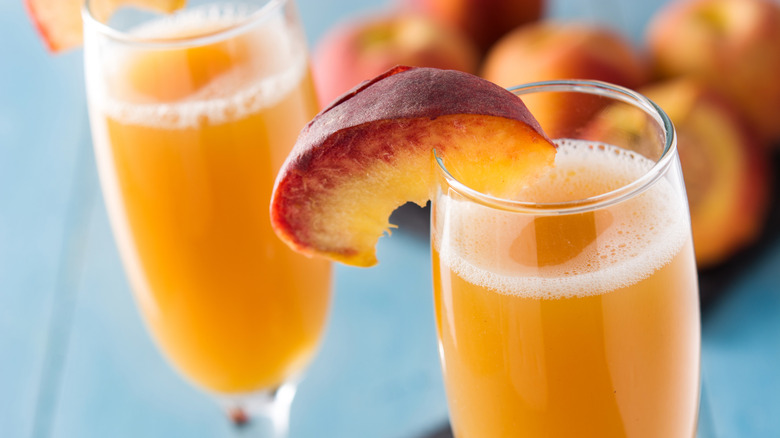 Δύο bellinis με ένα jigger, μισή ροδάκινα, και ένα φελλό κρασιού όλα πάνω από ένα λευκό πανί σε ένα ξύλινο τραπέζι