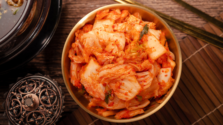 Ένα μπολ γεμάτο kimchi με chopsticks, ένα μπολ με φαγητό και άλλα αντικείμενα στο τραπέζι.
